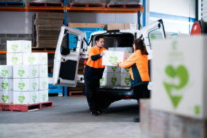 A woman passes a Good360 box to a man as they stack them into the back of a white van.