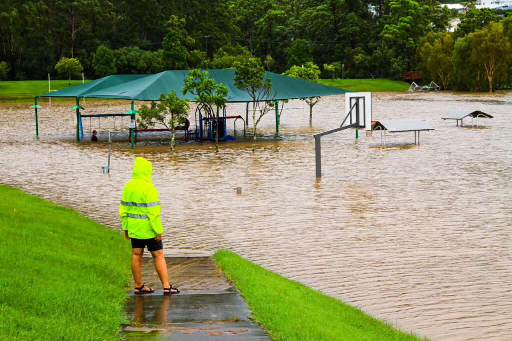 A person in high vis with their back to the camera stands looking at a flooded park