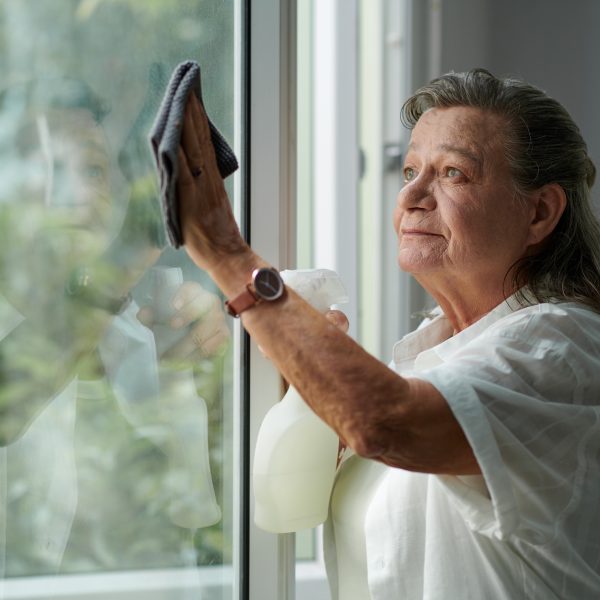 Senior woman wiping dirty window in her apartment